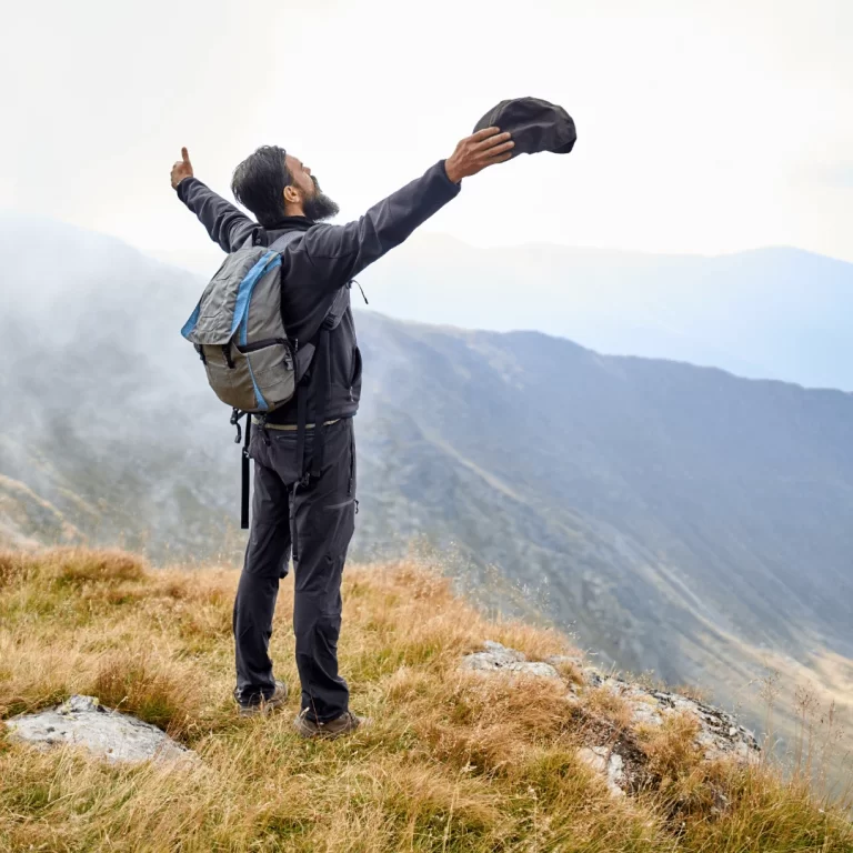 Man with beard outside on overlook with arms out, having conquered addiction.