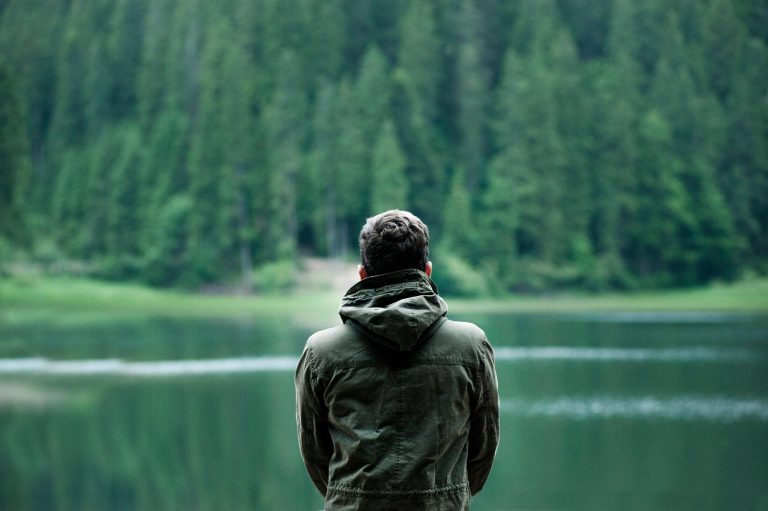 Back of a man looking over a calm lake having conquered drug and alcohol addiction.