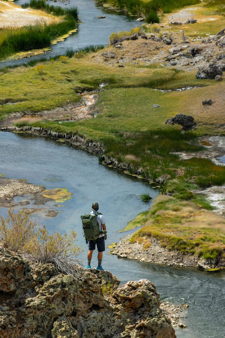 Man with back pack standing on rock looking at winding river having overcome Addiction.
