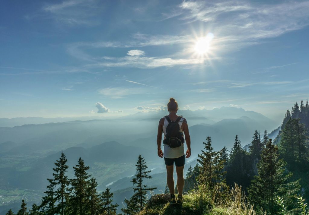 Man with backpack overlooking valley floor from edge of the mountain feeling accomplished from conquering drug and alcohol addiction.
