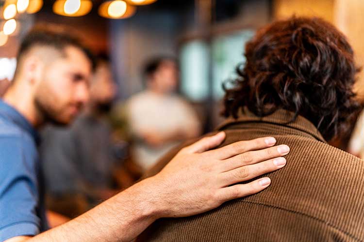 Man with hand on the back consoling another man with his alcohol addiction.
