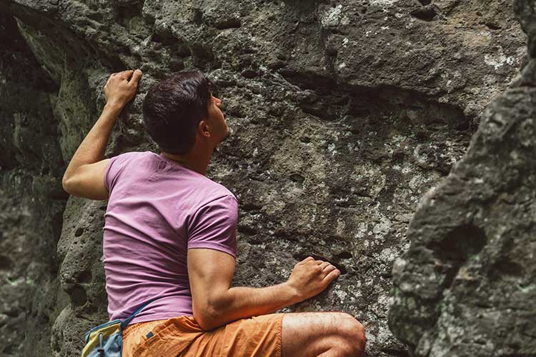 Man climbing a rough rock wall to overcome addiction.