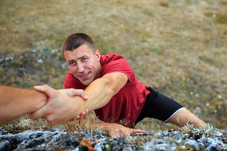 Man reaching and being helped up by another man while outdoors in wilderness therapy.