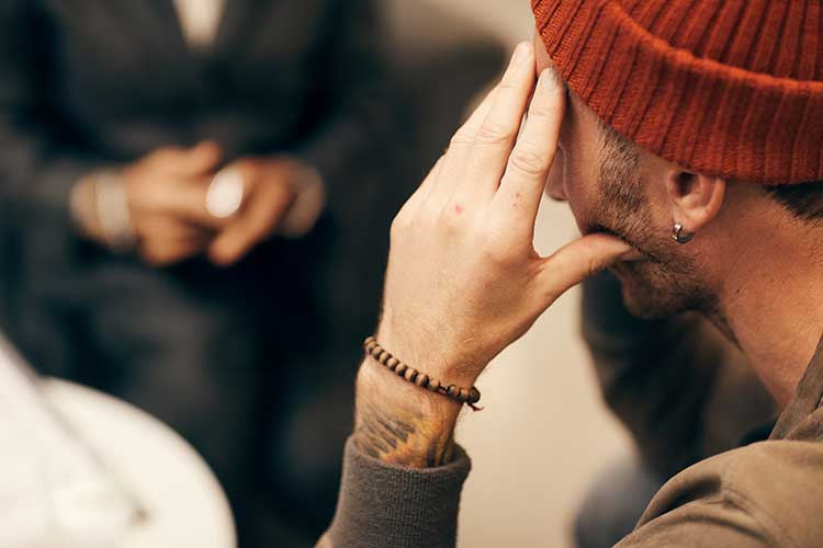 Young man with hands on head talking with a therapist.