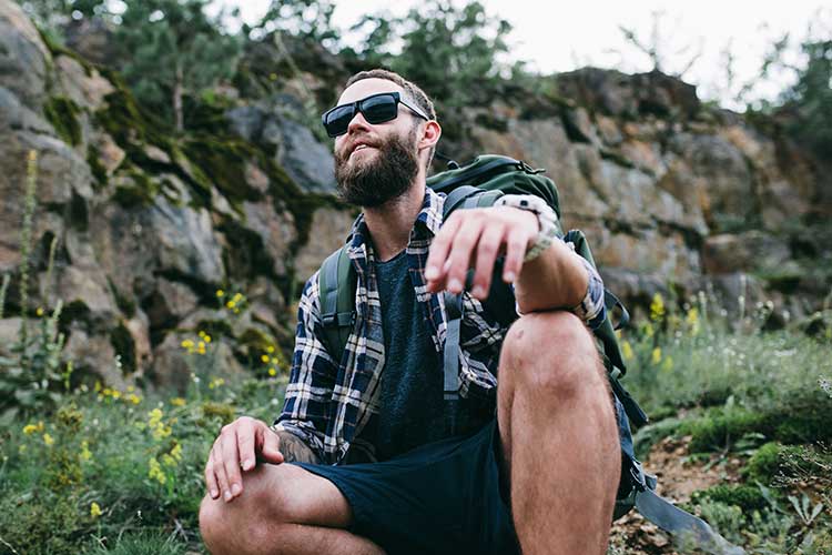 Man squatting outside with rock wall behind participating in wilderness therapy.