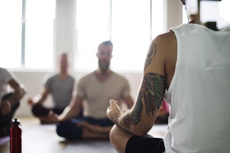 Men in Yoga class sitting in lotus position during wellness coaching for addiction recovery in Vista, CA.