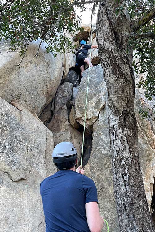Below view of man rock climbing as part of the outdoor process of addiction treatment in Vista, CA.