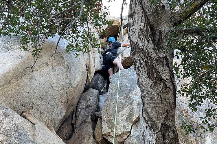 Below view of man rock climbing as part of the outdoor process of addiction treatment in Vista, CA.