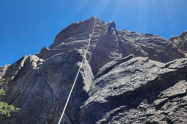 Below view of man rock climbing as part of the outdoor process of addiction treatment in Vista, CA.