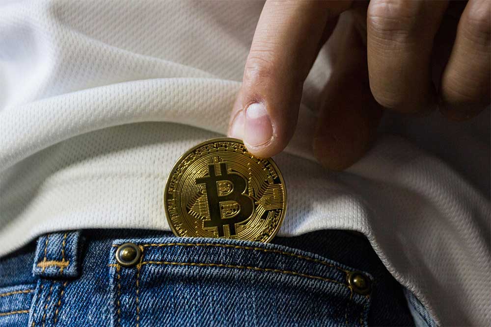 Photos os bitcoin being placed inside jean pocket a visual metaphor of accepting bitcoin payment at Sacred Journey addiction treatment facility.