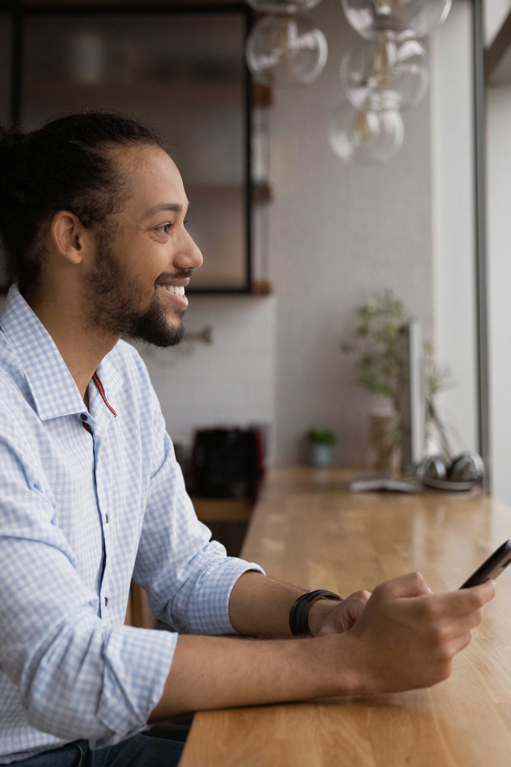 Man in his kitchen looking out window and at his phone for online rehab.